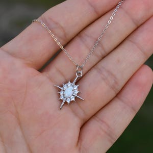 A hand holding a delicate silver necklace with a star-shaped pendant.
