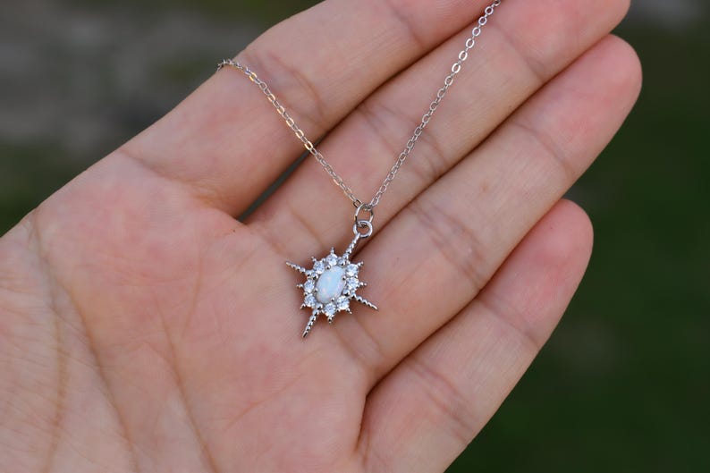 A hand holding a delicate silver necklace with a star-shaped pendant.
