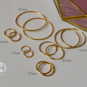May include: A collection of gold-colored hoop earrings in various sizes, ranging from 15mm to 50mm in diameter. A US quarter is included for size comparison. The earrings are arranged on a white surface.