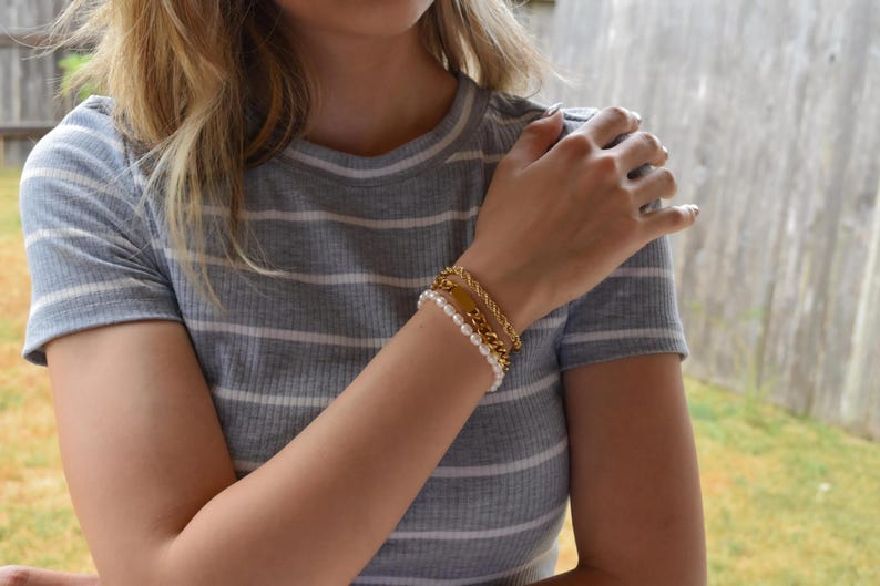 A close-up of a person's arm wearing a gray and white striped shirt, with a bracelet and multiple rings on their fingers.
