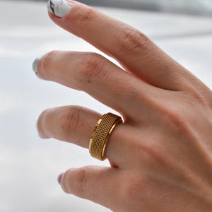 A close-up of a person's hand wearing a gold ring with a textured band.
