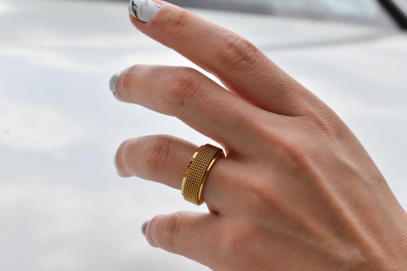 A close-up of a person's hand wearing a gold ring with a textured band.