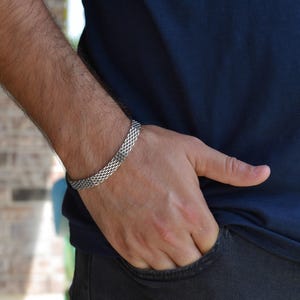 A close-up view of a person's hand wearing a silver bracelet, with their hand resting in their pocket.