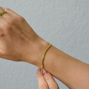 A close-up view of a person's hand wearing a gold bracelet and ring against a plain white background.