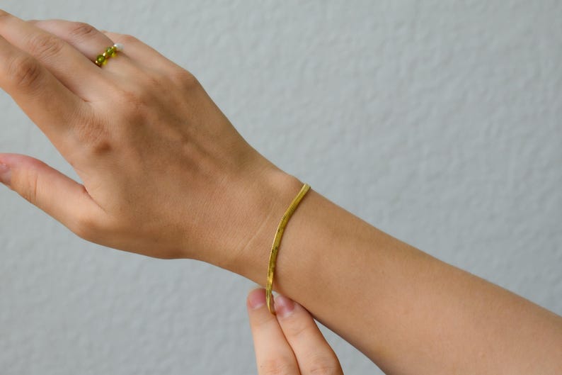 A close-up view of a person's hand wearing a gold bracelet and ring against a plain white background.