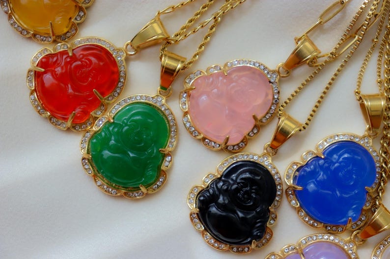 A collection of ornate gold necklaces with colorful pendants, including a green Buddha, a pink Buddha, and other vibrant designs.