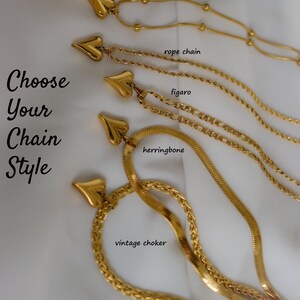 a variety of gold-colored necklaces with heart-shaped pendants, each with different chain styles such as beaded, snake, rope, figuro, herringbone, and vintage choker.