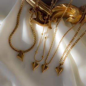 a collection of gold necklaces with heart-shaped pendants, arranged on a white fabric surface.