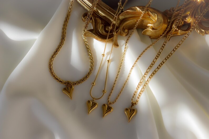 a collection of gold necklaces with heart-shaped pendants, arranged on a white fabric surface.