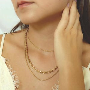 A close-up of a woman's neck and chest area, with multiple gold necklaces visible.