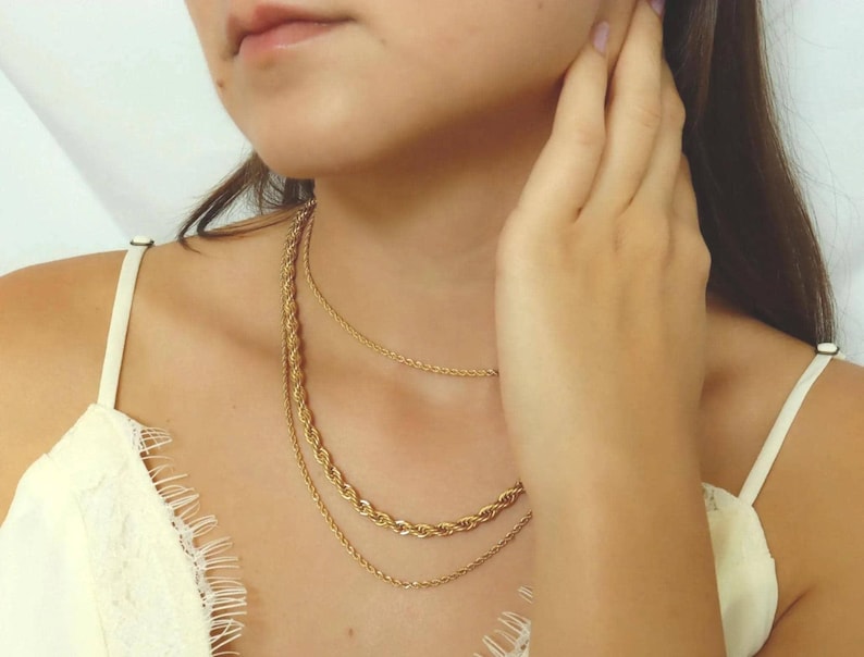 A close-up of a woman's neck and chest area, with multiple gold necklaces visible.