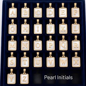 a collection of gold-colored alphabet pendants arranged in a grid-like pattern on a dark background.