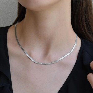 A close-up of a woman wearing a silver necklace with a long, thin chain.