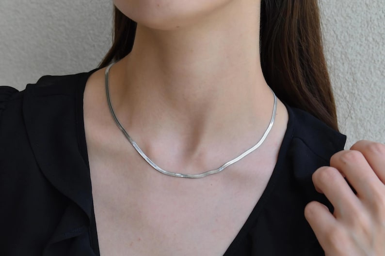 A close-up of a woman wearing a silver necklace with a long, thin chain.