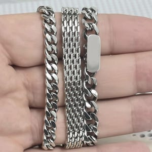A person's hand holding three silver-colored metal bracelets.