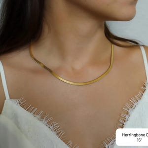 A close-up of a woman wearing a gold necklace with a thin, long chain.