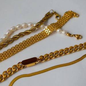 a collection of gold necklaces and bracelets arranged on a white background.