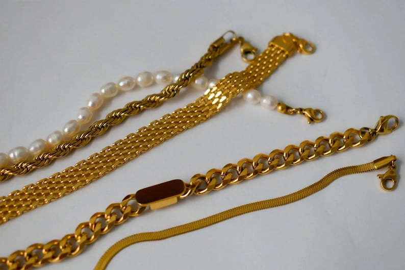 a collection of gold necklaces and bracelets arranged on a white background.