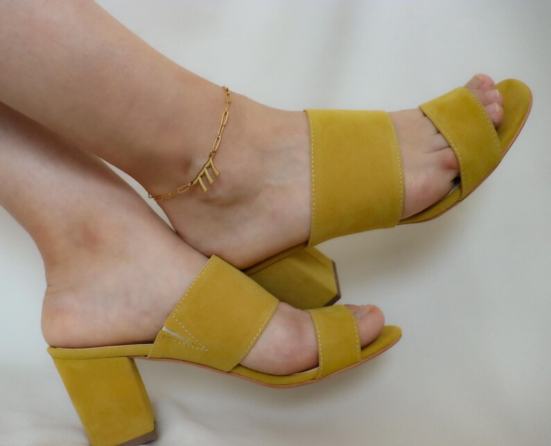 A pair of yellow high-heeled sandals with a gold ankle bracelet.