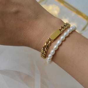 A gold bracelet with a chain and a pearl bracelet on a person's wrist.