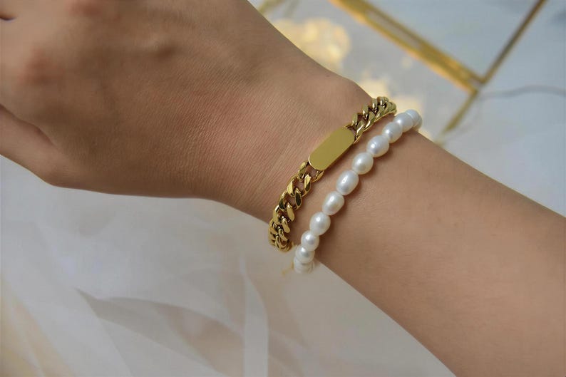 A gold bracelet with a chain and a pearl bracelet on a person's wrist.