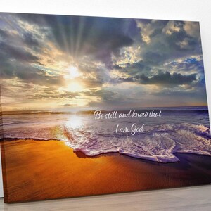 Può includere: Stampa su tela raffigurante una scena di spiaggia al tramonto. L'immagine mostra un cielo vibrante con nuvole, i raggi del sole e le onde dell'oceano. Il testo sulla tela recita: "Fermatevi e sappiate che io sono Dio."