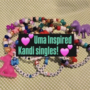 May include: A collection of colorful beaded bracelets with the text "Uma Inspired Kandi singles!" and heart graphics. The bracelets feature various colors and include small plastic charms of a horse and a unicorn.