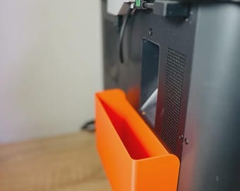 Könnte beinhalten: Ein orangefarbener, rechteckiger Aufbewahrungsbehälter, der an der Rückseite eines schwarzen elektronischen Geräts befestigt ist. Der Behälter ist auf einer Holzoberfläche montiert. Kabel und Anschlüsse sind sichtbar.