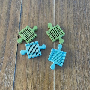 May include: Four colorful puzzle pieces in shades of green and blue are arranged on a wooden surface. Each piece has a unique shape with a series of parallel lines, suggesting a construction or building toy.
