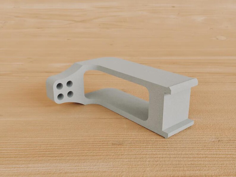May include: A light grey, geometric object featuring four circular holes on one end. It has a rectangular aperture and rests on a wooden surface. The design is modern and minimalist.