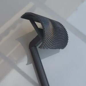 May include: A dark gray, 3D-printed object with a handle and a curved, ridged head. The object appears to be a tool or a decorative item, possibly for home decor or a craft project.