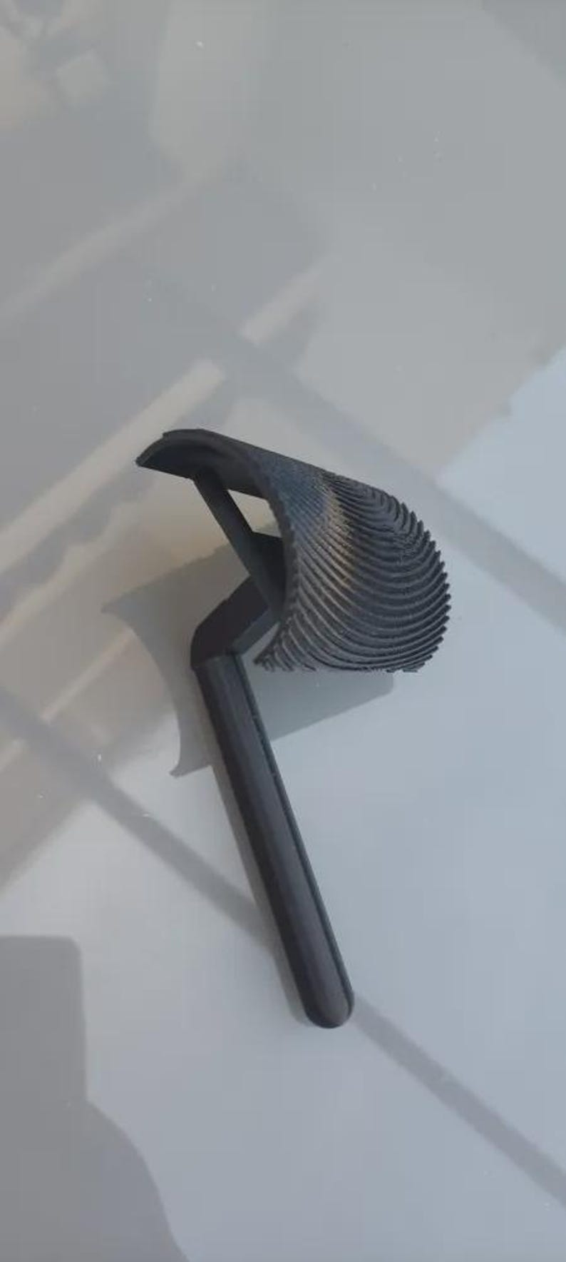 May include: A dark gray, 3D-printed object with a handle and a curved, ridged head. The object appears to be a tool or a decorative item, possibly for home decor or a craft project.