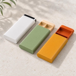 Puede incluir: Tres cajas de almacenamiento rectangulares deslizantes con bordes redondeados. Una caja es blanca con tapa negra, otra es verde salvia con bandeja interior beige y otra es amarillo mostaza con bandeja interior naranja, cada una con dos compartimentos.
