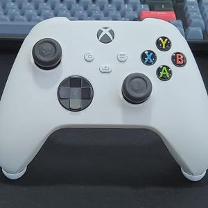 Può includere: Un controller bianco Xbox Series X/S con levette nere e un D-pad. Il controller presenta pulsanti azione colorati (verde A, rosso B, blu X, giallo Y) e un logo Xbox centrale. Progettato per il gaming.
