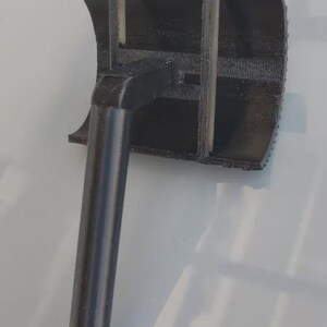 May include: A black 3D-printed object with a cylindrical handle and a rectangular head. The head has a curved top and internal supports. The handle is metallic gray.