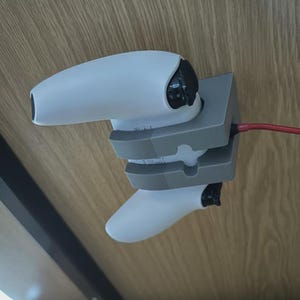 Può includere: Un controller di gioco bianco è montato sotto una superficie di legno con una staffa grigia. Un cavo rosso si estende dalla staffa. Il controller è bianco con dettagli neri.