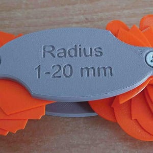 May include: A grey radius gauge with orange blades. The gauge reads "Radius 1-20 mm". The blades are arranged in a fan shape, and the gauge is secured with two screws. The tool is used for measuring curves.