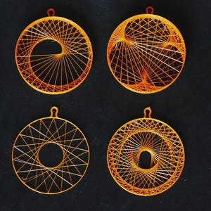 Può includere: Quattro ornamenti circolari arancioni con intricati disegni di string art. Ogni ornamento ha un motivo diverso, con un piccolo anello rosso in alto per appenderlo. Lo sfondo è nero pieno.