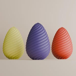 May include: Three egg-shaped ornaments in yellow, purple, and red. Each has a textured, spiral pattern. The objects are set against a neutral backdrop, creating a simple and elegant composition.
