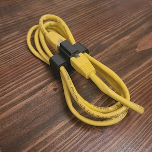 May include: A coiled yellow Ethernet cable with black connectors. The cable is labeled with white text, including "ETL Verified" and "DUCTORK". The cable is on a dark wood surface.