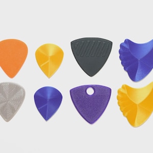 May include: A collection of eight guitar picks in various shapes and colors. The picks include orange, yellow, black, blue, and purple. Some picks have textured surfaces or unique designs, while others are smooth.