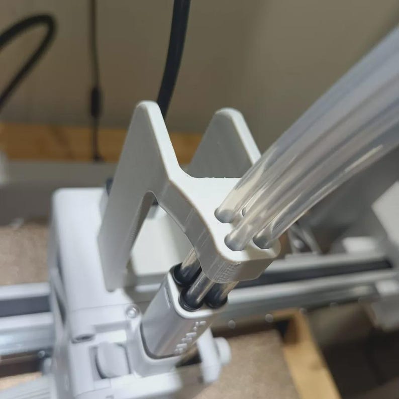 May include: A close-up shot of a white 3D-printed component with clear tubes. The component has a geometric design with a support structure. The clear tubes are flexible and made of plastic. The image is well-lit.