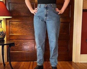 May include: A pair of light blue denim jeans with a high waist and a straight leg fit. The jeans are worn by a person standing in front of a wooden door.