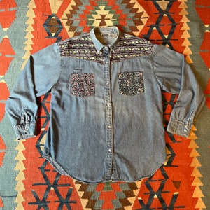 May include: A blue denim shirt with floral embroidery on the yoke and pockets. The shirt has a button-down collar and long sleeves.