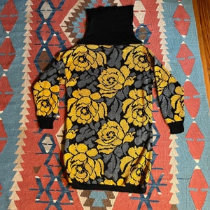 May include: A black turtleneck sweater with a yellow and gray floral pattern. The sweater has long sleeves and a loose fit.