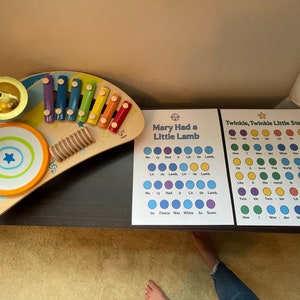 May include: A wooden toy xylophone with rainbow coloured keys, a small drum, and a bell. Two printable charts for learning the lyrics to the songs "Mary Had a Little Lamb" and "Twinkle, Twinkle Little Star" with colourful dots representing each word.