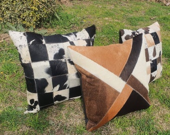 May include: Three decorative throw pillows with a patchwork design made from cowhide. The pillows are in black, white, brown, and tan colors.
