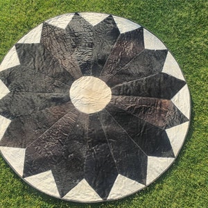 Może przedstawiać: Okrągły dywan z czarno-białej skóry krowiej z wzorem gwiazdy. Dywan jest wykonany ze skóry i ma naturalny, rustykalny wygląd.