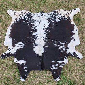 May include: Black and white cowhide rug with a spotted pattern. The rug is made from natural cowhide and has a soft, supple texture.