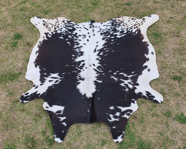 May include: Black and white cowhide rug with a spotted pattern. The rug is made from natural cowhide and has a soft, supple texture.